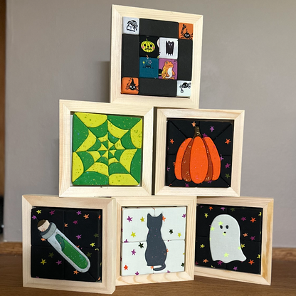 A set of five small square framed art prints with a Halloween theme, stacked in a pyramid on a wooden mantel against a gray wall.