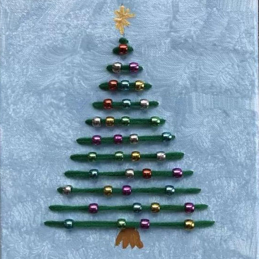 A handmade Christmas tree decoration made from green yarn stripes and shiny multicolored beads, topped with a gold star and finished with a gold bow at the bottom, set against a light blue textured fabric background.